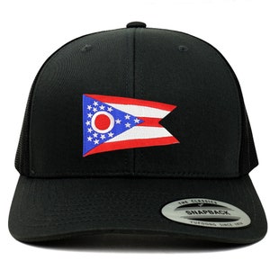 Può includere: Un cappello da camionista nero con una toppa della bandiera dello stato dell'Ohio in rosso, bianco e blu sul davanti. Il cappello ha una parte posteriore in rete nera e una chiusura a scatto nera. Il cappello ha anche un adesivo bianco sul retro che dice "The Classics" e "Snapback" con il logo Yupoong.