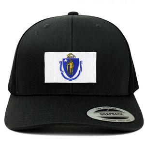 May include: Black trucker hat with a white patch featuring the state flag of Massachusetts. The flag has a blue shield with a gold star and a man holding a sword. The hat has a black mesh back and a black snap closure. The hat has a sticker on the back that says "The Classics Snapback Yupoong Since 1974."