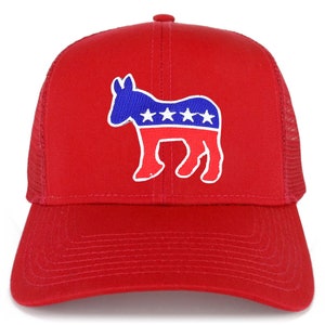 Op de afbeelding: Rode trucker cap met een wit silhouet van een ezel die een Amerikaans vlagontwerp in blauw en rood draagt. De ezel heeft vijf witte sterren op de rode streep.