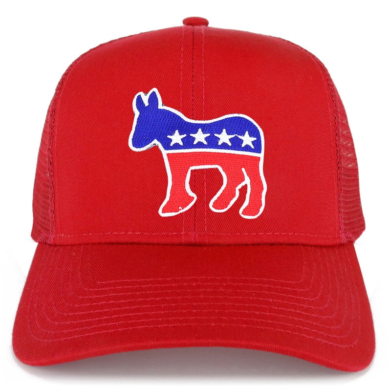 Op de afbeelding: Rode trucker cap met een wit silhouet van een ezel die een Amerikaans vlagontwerp in blauw en rood draagt. De ezel heeft vijf witte sterren op de rode streep.