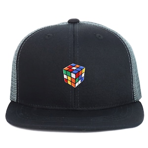 Op de afbeelding: Een zwarte en grijze truckercap met een kleurrijk Rubik's Cube geborduurd op de voorkant.