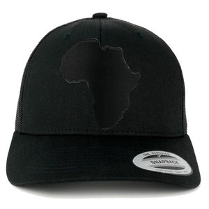 May include: Black trucker hat with a black outline of the continent of Africa on the front. The hat has a black mesh back and a black snap closure. The hat has a white label on the back that says "The Classics" and "Snapback" with the Yupoong logo.