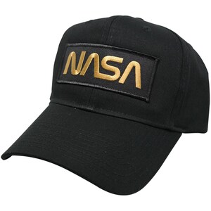 Puede incluir: Una gorra de béisbol negra con un parche de la NASA bordado en oro en la parte delantera.