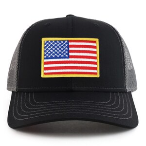 May include: A black and grey trucker hat with a red, white and blue American flag patch on the front. The flag patch has a yellow border.