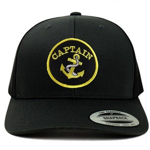 May include: Black trucker hat with a yellow embroidered patch that says "CAPTAIN" with an anchor inside the circle. The hat has a black mesh back and a black snap closure.
