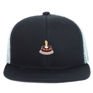 May include: A black and white trucker hat with a birthday cake embroidered on the front. The cake is brown with pink frosting and a lit candle.
