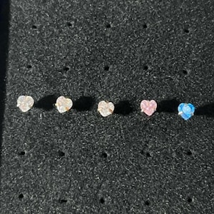 May include: Five heart-shaped earrings with clear and colored crystals. The earrings are displayed on a black background.