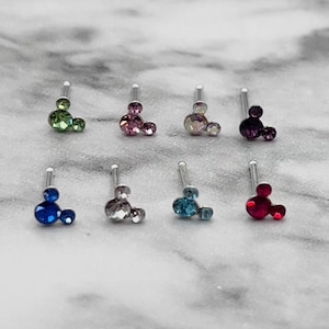 May include: Eight silver nose rings with a Mickey Mouse design featuring different colored rhinestones. The colors include green, pink, iridescent, purple, blue, light blue, and red.