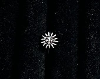May include: A silver-toned ring featuring a central sun motif. The sun design includes a detailed face in the middle surrounded by radiating, pointed rays that extend outward in a circular pattern. The metal has a polished, reflective finish.