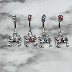 Pode incluir: Quatro an&eacute;is de umbigo de prata com pingentes de escorpi&atilde;o. Cada anel tem uma pedra preciosa de cor diferente: rosa, azul, azul claro e vermelho.