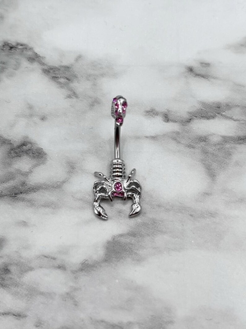 Pode incluir: Anel de umbigo de prata com design de escorpi&atilde;o e gemas rosa.