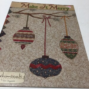 May include: A quilted Christmas wall hanging with the text "Make It Merry" above three hanging ornaments. The ornaments are decorated with the words "Peace on Earth" and "Believe". The background is a beige color with a swirling pattern.