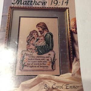 May include: A Leisure Arts cross-stitch pattern leaflet titled Matthew 19:14 by Carol Emmer. The cover features a framed needlework design of a figure with long hair holding three children, with the text Suffer little children, and forbid them not.