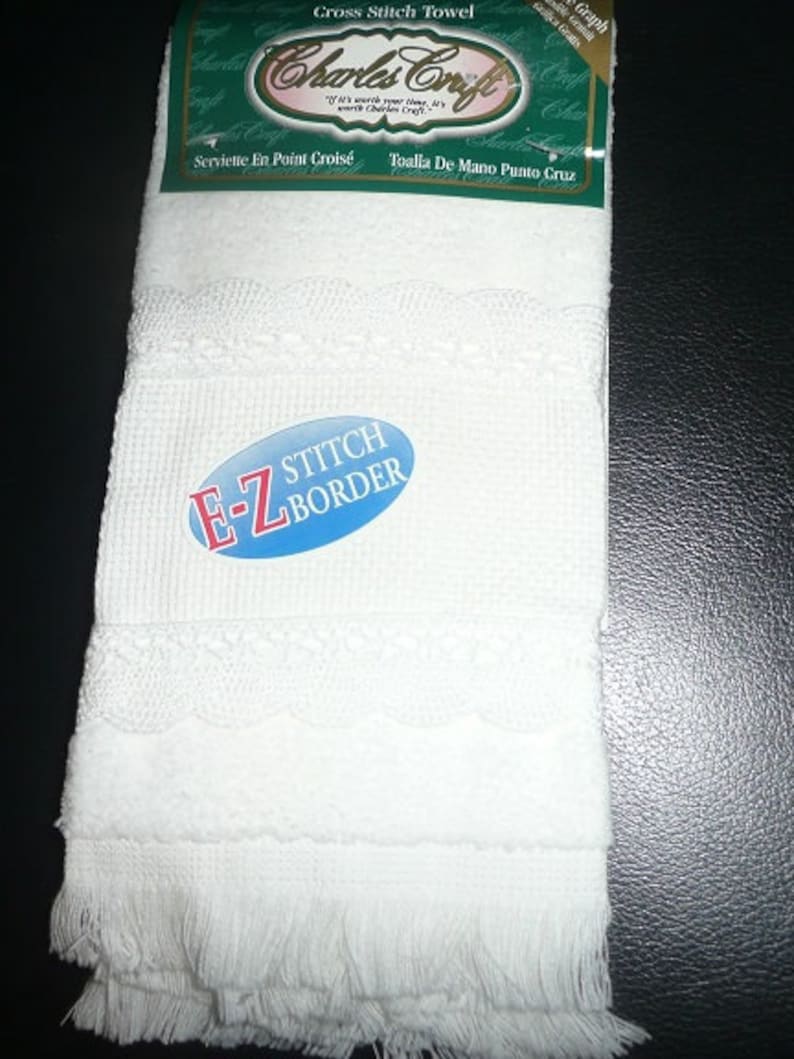 Puede incluir: Toalla blanca de punto de cruz con borde de encaje festoneado y flecos. La toalla tiene el texto "Charles Craft" y "E-Z Stitch Border" en el embalaje.