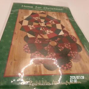 May include: A sewing pattern package titled Home for Christmas featuring two patchwork tree skirts in red, green, and cream fabrics. The packaging displays a finished star-shaped skirt and a scalloped-edge skirt on a wood-grain background.