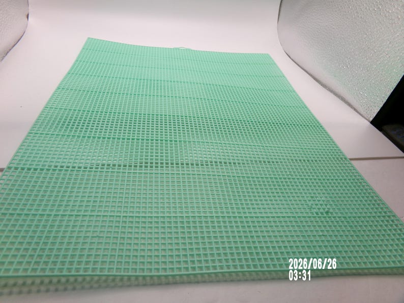 May include: A rectangular mint green plastic canvas sheet featuring a uniform grid of small square holes throughout its surface. The material is rigid and flat, designed for needlepoint or craft projects, with the date 2026/06/26 03:31 printed in white.