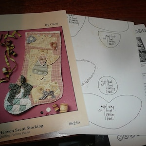 May include: A Heaven Scent Stocking quilting pattern packet by Cheri, number 6263. The packet includes a color photograph of a finished quilted stocking with angel motifs, buttons, and ribbons, alongside white paper templates with handwritten instructions.