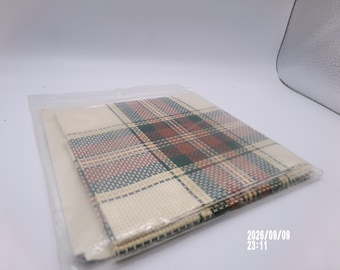 May include: A square piece of fabric featuring a plaid pattern in shades of cream, dark green, and deep red, enclosed in a clear plastic sleeve. The textile has a visible woven grid texture and is folded neatly within the protective packaging.