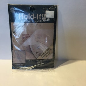 May include: A white needlework stabilizer called "Hold-It!!" is packaged in a clear plastic bag. The product is 20 inches by 22 inches (50.8 cm x 55.9 cm) and is described as "firm".