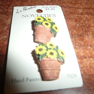 May include: Two novelty buttons featuring miniature terracotta flower pots filled with yellow sunflowers and green leaves. The buttons are hand-painted and attached to a white card labeled "Le Bouton Novelties".