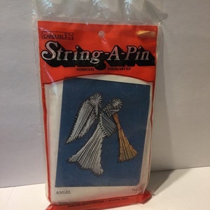 May include: A complete String-A-Pin string art kit in a clear plastic bag. The kit features an angel design on a blue background. The packaging is red and white with the text "String-A-Pin" and "Angel".