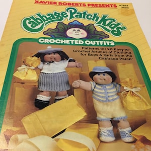 May include: A vintage Cabbage Patch Kids crochet pattern book. The cover features two dolls in crocheted outfits, with the text "CROCHETED OUTFITS" and "Patterns for 20 Easy-to- Crochet Articles of Clothing for Boys & Girls from the Cabbage Patch". The background is yellow.