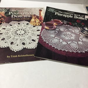 May include: Two crochet pattern books featuring pineapple doilies. The book on the left is titled "Heirloom Pineapple Doilies" with the text "6 designs in thread" and "by Trish Kristoffersen". The book on the right is titled "The Ultimate Book of Pineapple Doilies".