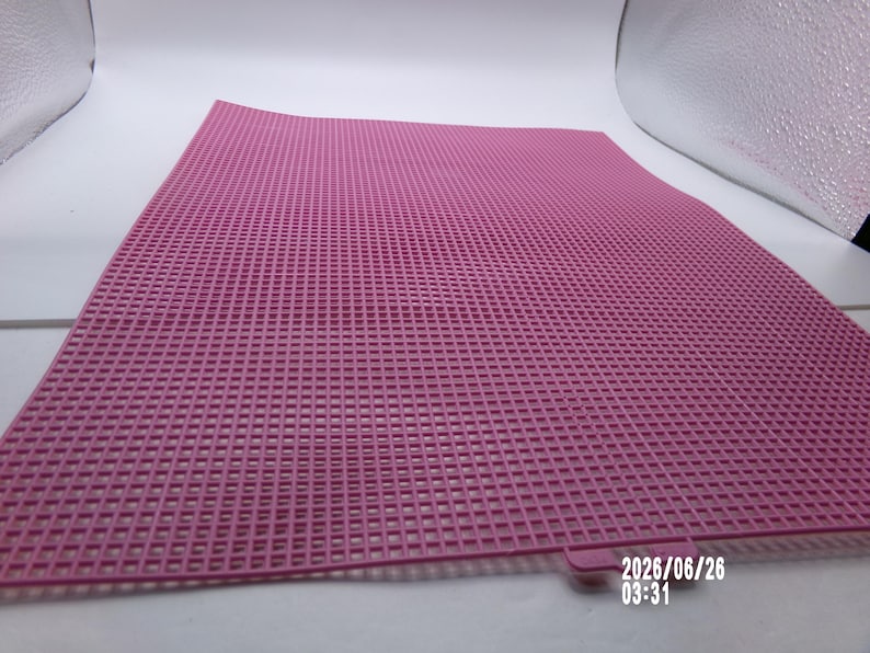 May include: A square pink plastic canvas sheet featuring a uniform grid of small, evenly spaced holes throughout its surface. A small tab extends from one edge, and the date 2026/06/26 03:31 is printed in white text in the bottom right corner.