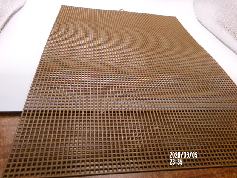 May include: A rectangular brown plastic canvas sheet featuring a uniform grid of small square holes throughout its surface. The material is rigid and flat, designed for needlepoint or crafting projects. The date 2026/06/05 23:35 is printed in white.