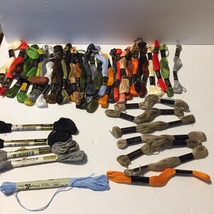 May include: A collection of embroidery floss in various colors, including green, orange, red, and blue. The floss is bundled and labeled, ready for crafting projects. The image shows a variety of shades and hues.
