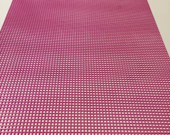 May include: A rectangular pink plastic canvas sheet featuring a uniform grid of small square holes throughout the entire surface. The sheet has a small, centered tab protruding from the top edge, designed for hanging or alignment purposes.
