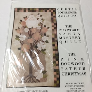 May include: A sealed package featuring a quilt pattern. The pattern includes a Santa Claus figure with a white beard and a pink dogwood tree design. Text on the package reads "The Old World Santa Mystery Quilt" and "The Pink Dogwood Father Christmas."