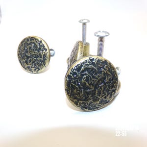 May include: A set of four bronze-colored cabinet knobs with a textured, circular design. Two knobs are attached to screws, while two are separate. The knobs have a dark, mottled appearance, suggesting an aged or antique finish.