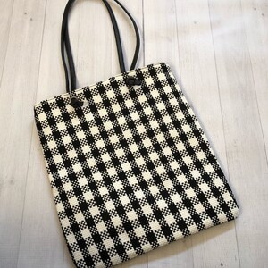 May include: Black and white checkered tote bag with black handles. The bag features a classic gingham pattern and a rectangular shape. The handles are attached with black accents.