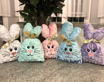 May include: Five plush Easter bunny bags in white, light blue, pink, blue, and purple. Each bag features embroidered bunny faces with pink noses and black whiskers. The blue bag has the name "Beckham" embroidered on it.