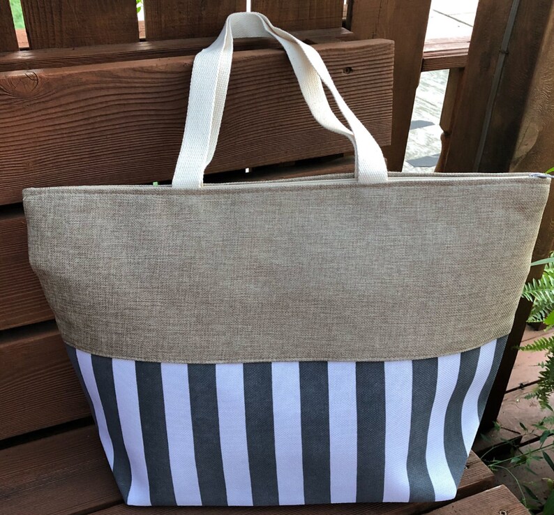 May include: A large, beige and white striped tote bag with a zipper closure. The bag has two white canvas straps.