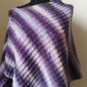 Może przedstawiać: Ponczo z dzianiny w paski w kolorze fioletowym, białym i szarym z diagonalnym wzorem.