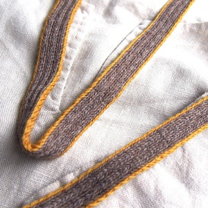 May include: A close-up of a brown and yellow fabric strap. The strap is woven with a brown and yellow thread.