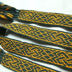 May include: Three woven green and gold bands with fringe ends. The bands have a geometric pattern.