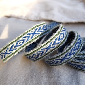 May include: Four woven bands with a geometric pattern in shades of blue and green. The bands are made of a soft, textured material and are arranged in a loose coil.