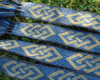 May include: Three woven fabric bands with a geometric pattern in shades of blue and gold. The bands are lying on a bed of green grass.