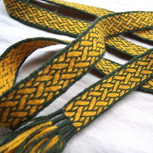 Può includere: Due cinturini intrecciati verde e giallo con una frangia intrecciata. I cinturini sono realizzati con un motivo di intreccio tradizionale.