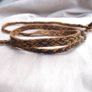 Peut inclure: Un cordon tissé brun et noir avec un motif géométrique. Le cordon est plié en deux et les extrémités sont nouées.