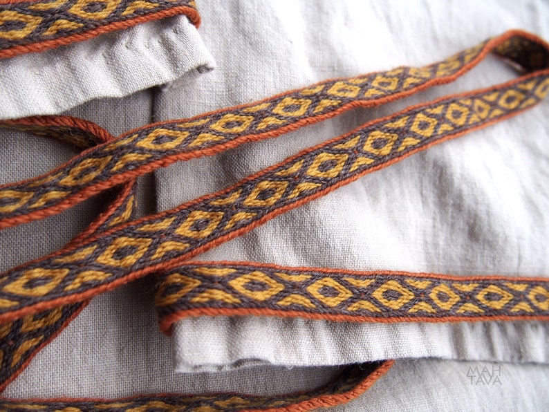 May include: Two brown and orange woven fabric straps with a geometric pattern. The straps are lying on a light beige fabric surface.