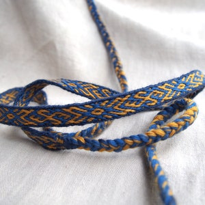 May include: A blue and gold braided cord with a geometric pattern. The cord is woven with a traditional technique and is perfect for crafting.