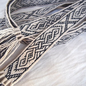 May include: A woven black and white belt with a geometric pattern and tassels on the ends.