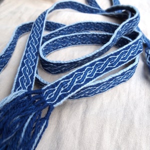 May include: A blue and white woven braid with tassels. The braid is made with a traditional pattern and is a beautiful example of handcraftsmanship.
