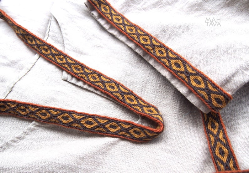May include: Close-up of a brown and black woven trim with a geometric pattern. The trim is on a light beige fabric.