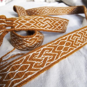 May include: A woven brown and white belt with a geometric pattern. The belt is made of a soft, natural material and has a fringed end.
