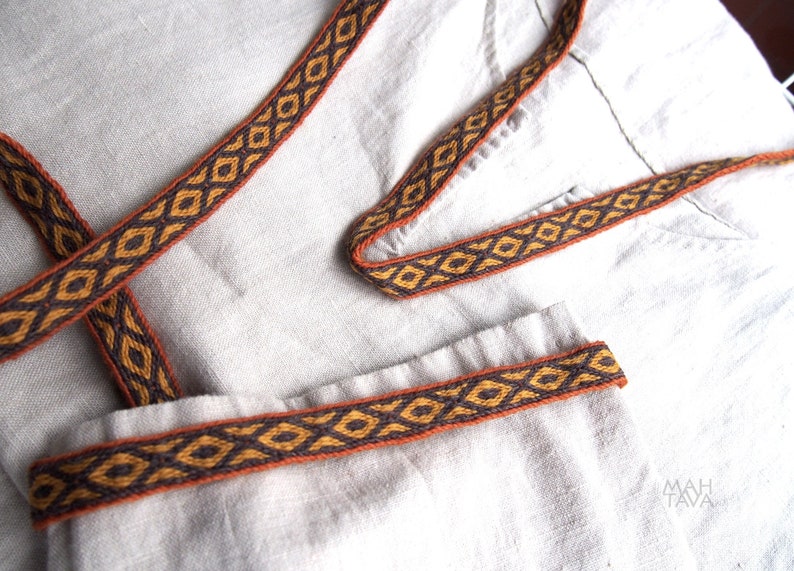 May include: A close-up of a white fabric with a brown and orange woven trim. The trim has a geometric pattern.